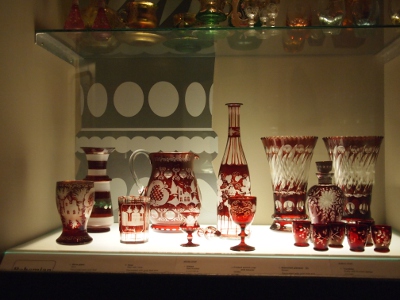 [Many pieces of red patterned crystal on a lit, glass shelf.]